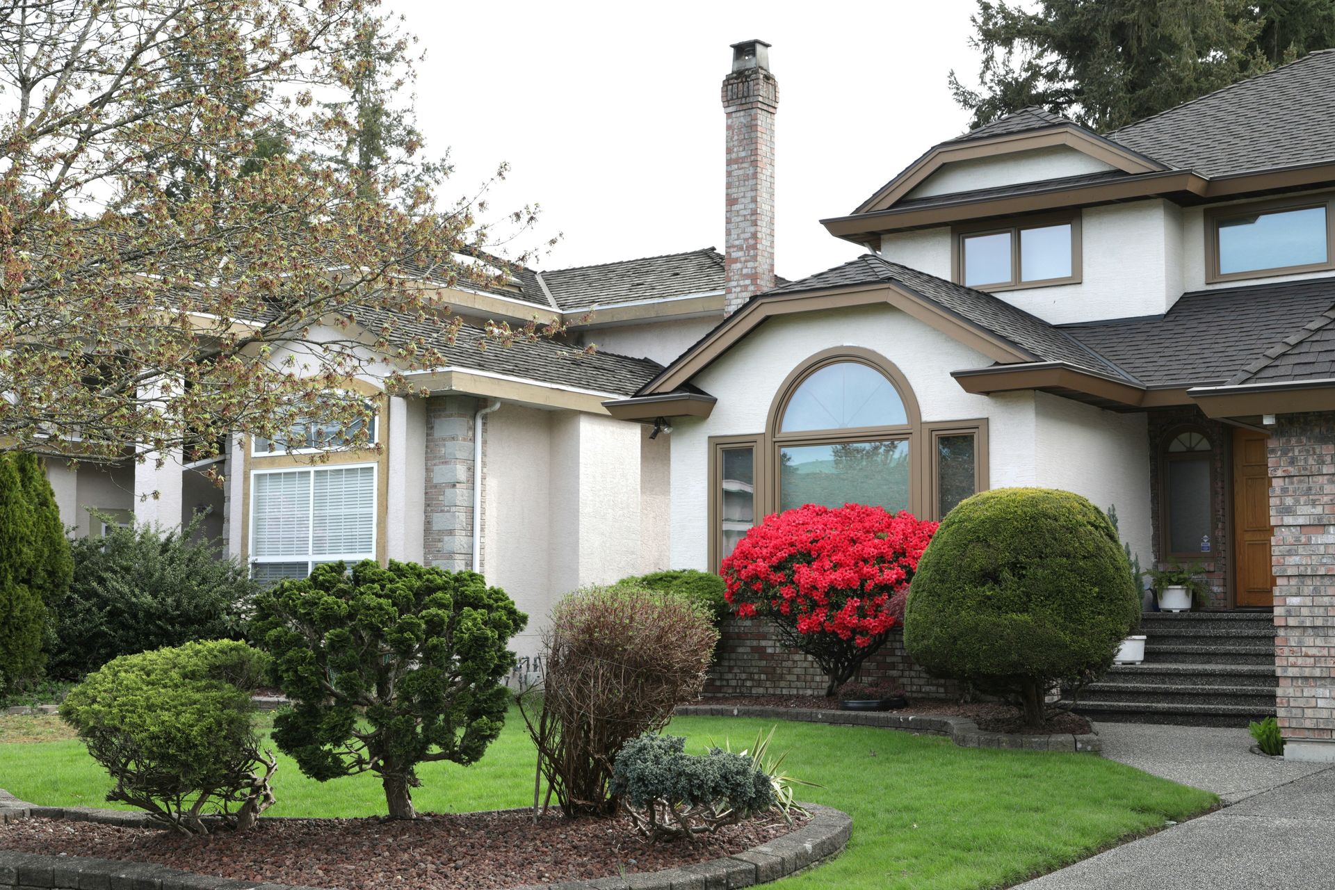 A large house with manicured bushes and red flowers.