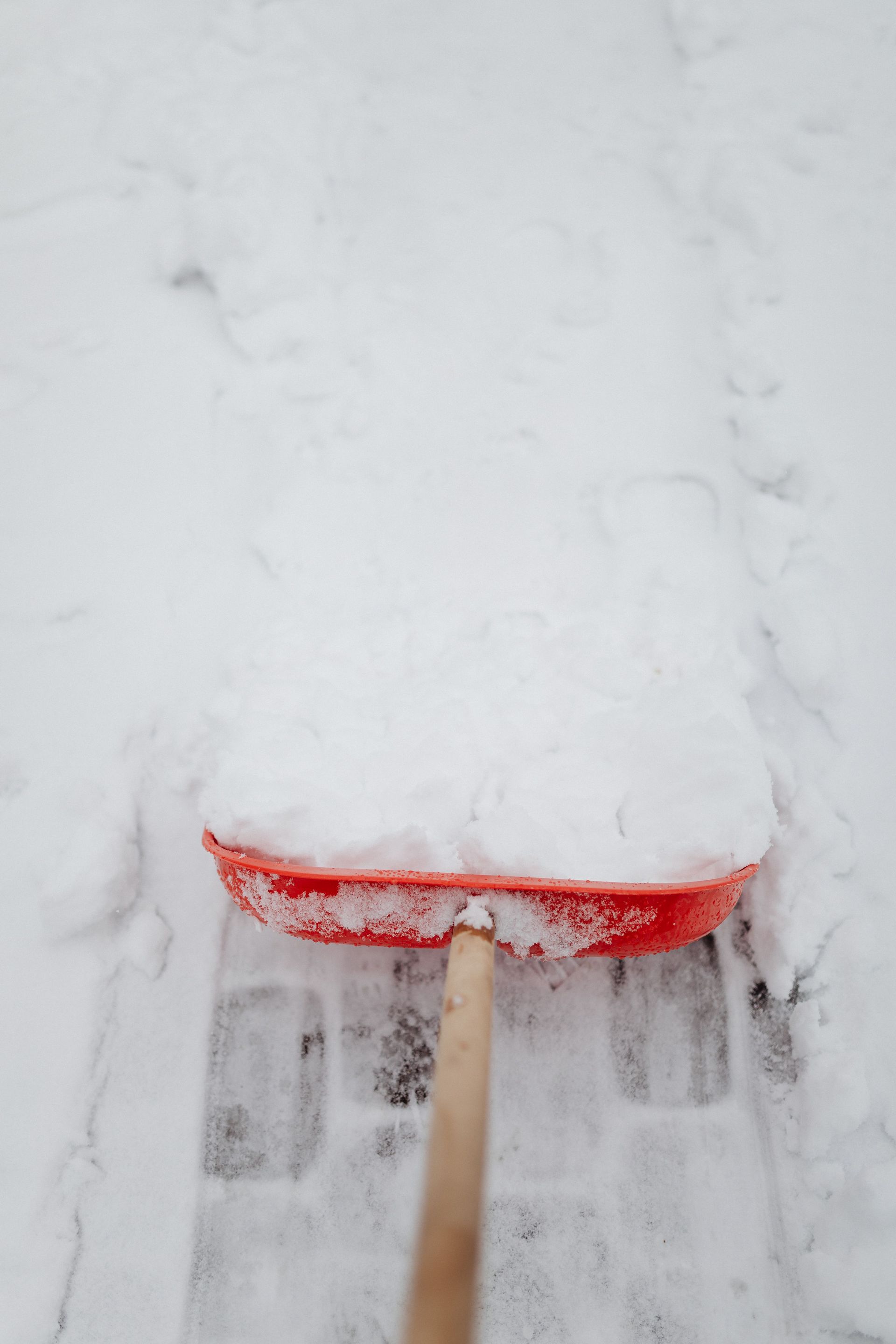 A red shovel moving snow off a path during winter, showcasing seasonal cleanliness.